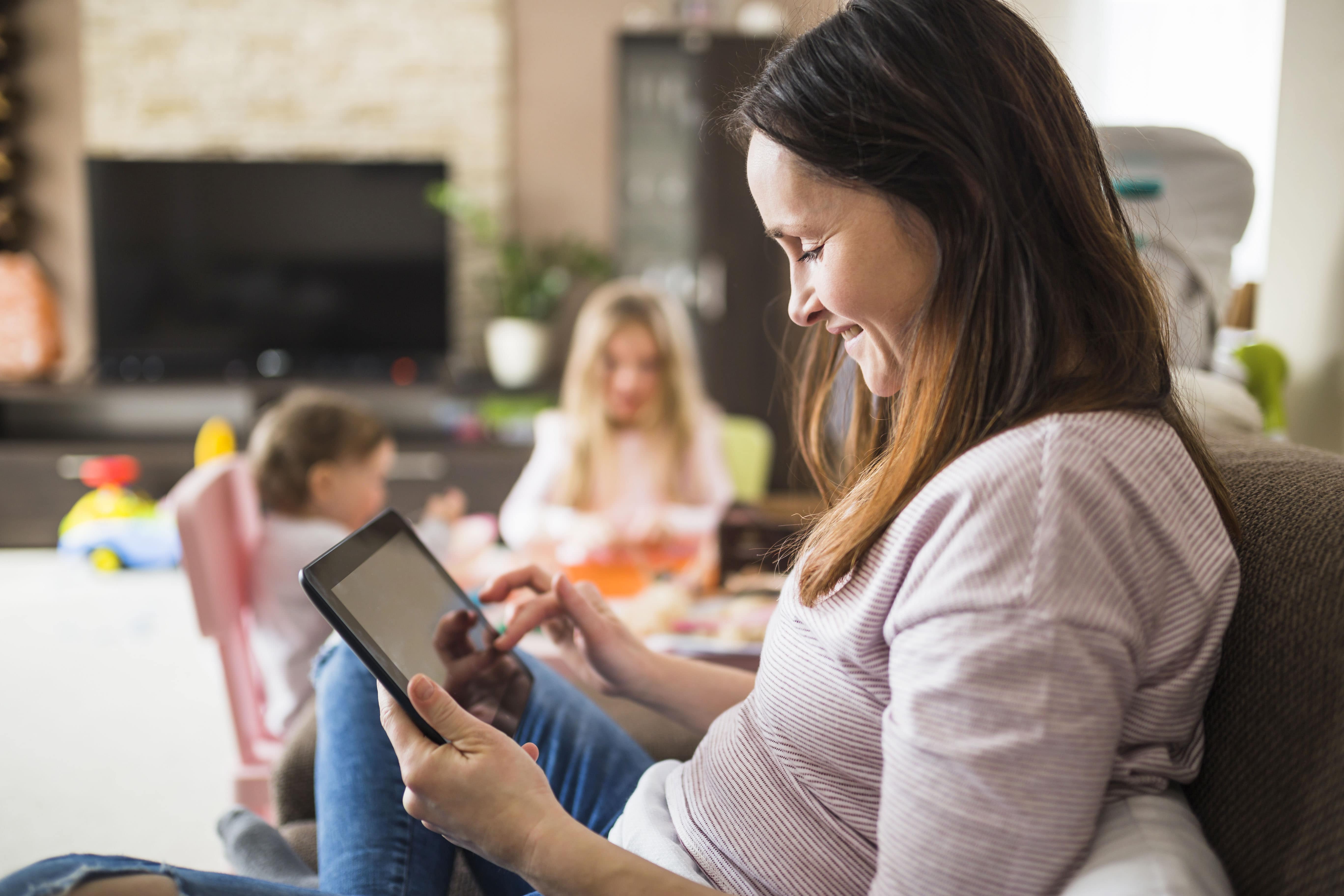 Madre consulta la tablet mientras sus hijos juegan