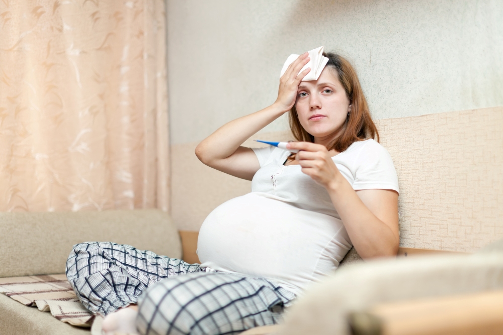 Dona embarassada amb febre mirant el termometre 