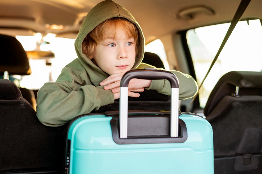 Nen a un cotxe amb una maleta de viatge